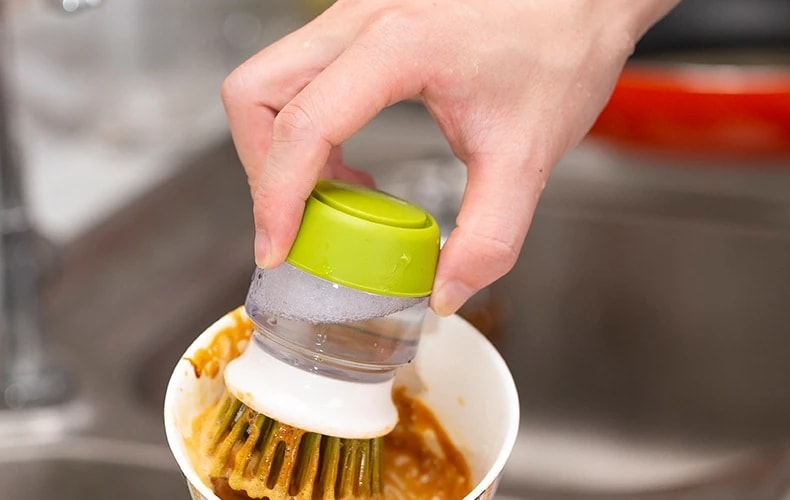 Hand holding the Jalenza soap dispensing dish brush over a bowl