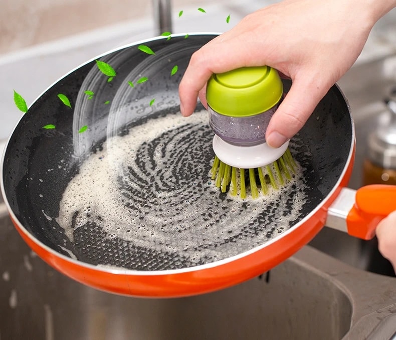 Hand scrubbing a frying pan with the Jalenza soap dispensing dish brush